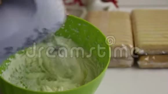 女人用奶油做蛋糕在装有搅拌器的塑料容器里旁边是一包萨沃亚迪饼干视频的预览图