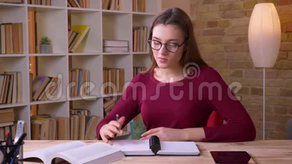 年轻的黑发女学生戴着眼镜看书在办公室里做笔记视频的预览图