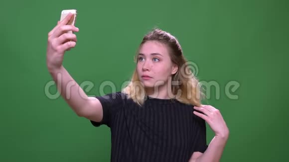 年轻漂亮的金发白种人女性在手机上自拍的特写照片背景与绿色隔离视频的预览图