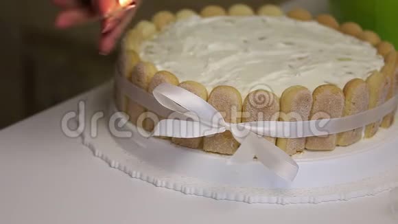 桌子上有一块萨沃亚迪饼干蛋糕用丝带绑着蝴蝶结女人用火柴把丝带的两端融化视频的预览图