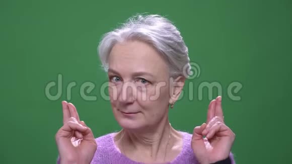 灰色头发的祖母穿着紫色的毛衣祈祷交叉的手指隔离在绿色的颜色背景上视频的预览图