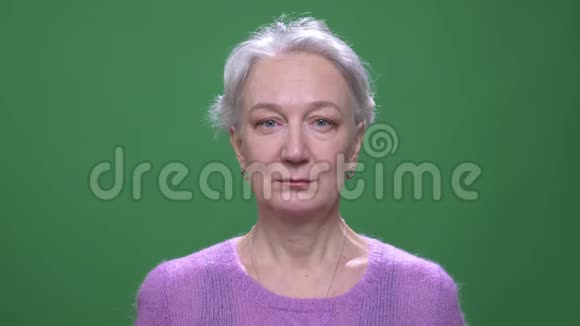 戴着紫罗兰色毛衣的灰发女人高兴地微笑着进入镜头隔离在绿色的彩色背景上视频的预览图