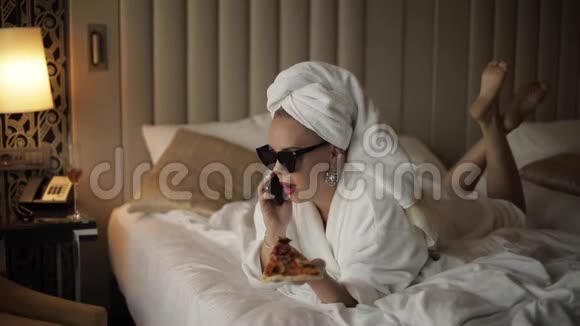 时尚女性淋浴后微笑着用智能手机说话躺在床上全镜头视频的预览图