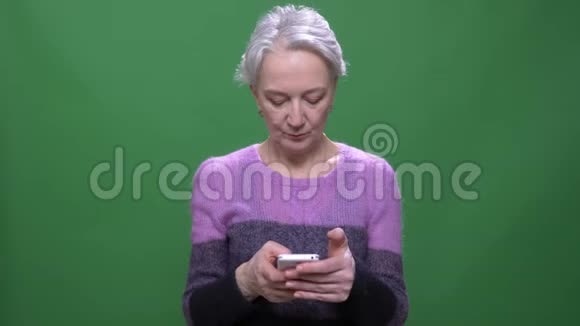 穿紫色毛衣的灰色头发的高级女性与智能手机一起工作隔离在绿色的色度背景上视频的预览图