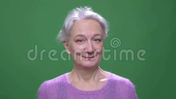 戴着紫罗兰色毛衣的灰黑头发的老女人在绿染色背景下的镜头中微笑着视频的预览图