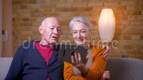 一对年长的白发白种人夫妇在平板电脑上开着网络视频卡在舒适的家里快乐而快乐视频的预览图