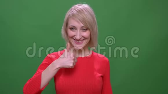 中年金发短发模特在绿色背景上做拇指上的手势视频的预览图