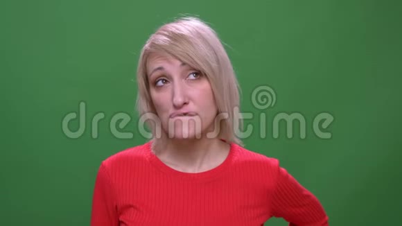 中年金发短发模特若有所思地咬着她的嘴唇孤立在绿色背景上视频的预览图