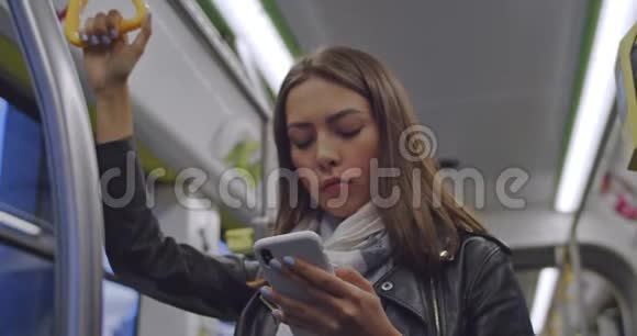 可爱的黑发女人的肖像抓住扶手在公共交通工具上发短信和浏览手机城市视频的预览图