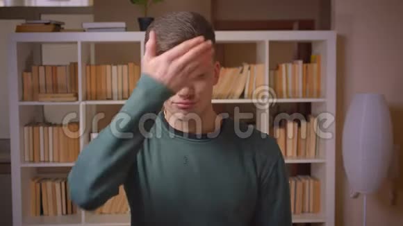 青年男学生手势的肖像在图书馆用手遮住脸视频的预览图