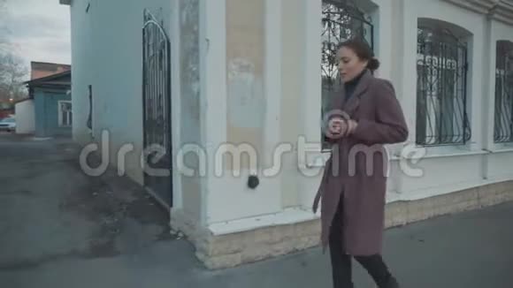 穿紫丁香外套的女孩走在旧城的街道上视频的预览图