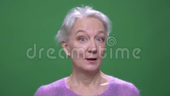 灰色头发的奶奶穿着紫罗兰色的毛衣在绿色的色彩背景下表现出娱乐和快乐视频的预览图
