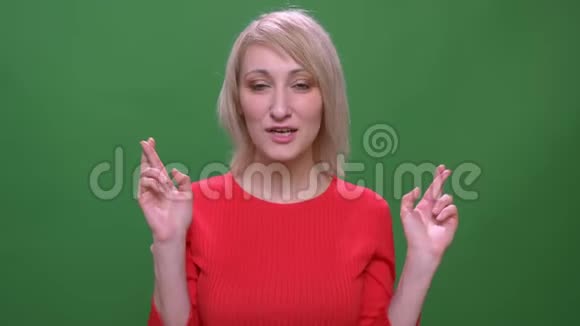 中年金发短发模特祈祷与交叉手指隔离在绿色背景视频的预览图