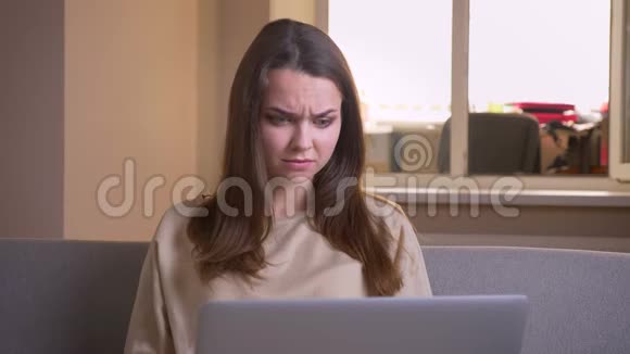 使用笔记本电脑和坐在沙发上看恐怖电影的年轻白种人女性特写镜头视频的预览图