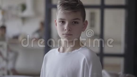 一个年轻男孩在镜头里看的肖像穿着白色t恤的没感情的男孩真正的人视频的预览图