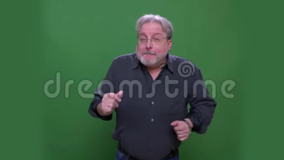 戴着灰色头发的美国高级男式眼镜跳舞在绿色的彩色背景下竖起大拇指视频的预览图