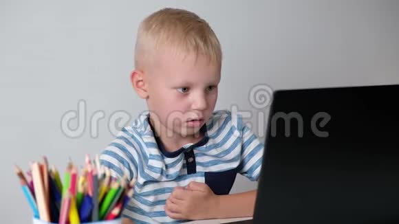 可爱的小男孩坐在桌子旁玩或在电脑上工作小学的孩子回学校去视频的预览图