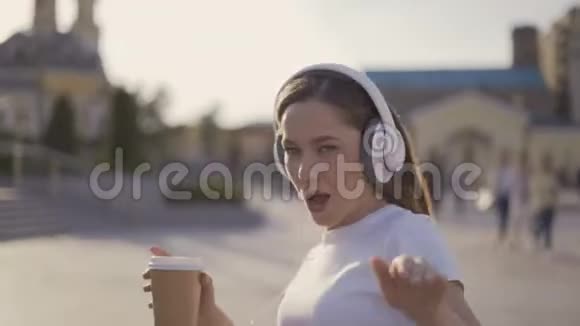 我快乐自由有趣的女孩在城里散步一大早戴着大耳机跳舞唱歌的女人视频的预览图