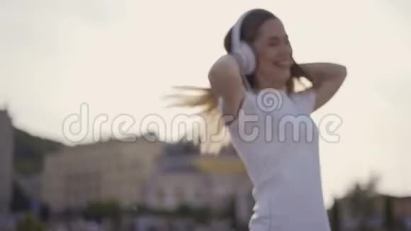 我快乐自由有趣的女孩在城里散步一大早戴着大耳机跳舞唱歌的女人视频的预览图