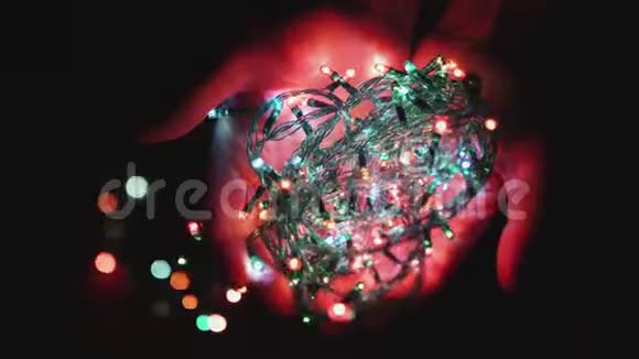 五颜六色的节日LED花环在黑暗背景下的女孩手中闪烁圣诞节的概念视频的预览图