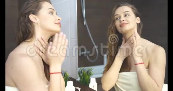 女人在浴室里对着镜子化妆时把奶油涂在皮肤上视频的预览图
