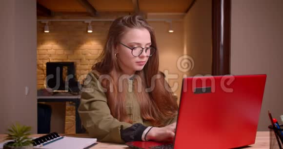 戴眼镜的年轻少女坐在办公室里用笔记本电脑工作的肖像视频的预览图