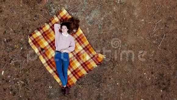 一位美丽的年轻女子躺在松林中央的地毯上照相机正平稳地移开视频的预览图