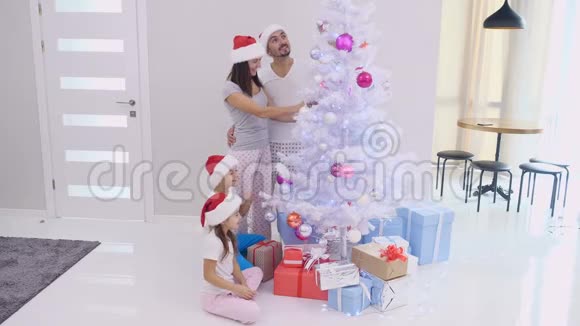 可爱的家人戴着圣诞帽在圣诞早晨装饰杉树视频的预览图