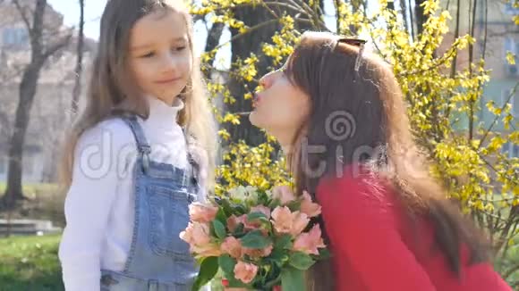 年轻的母亲穿着红衬衫正从她金发的小女儿手中接过一束五颜六色的鲜花亲吻她视频的预览图