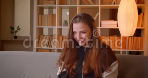 年轻的少女戴着3d眼镜看电视上的喜剧在家里的书架背景上开怀大笑视频的预览图