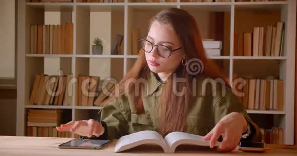 年轻女学生阅读书籍和在平板电脑上搜索信息的肖像在图书馆做作业视频的预览图