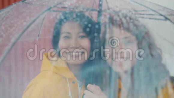 快乐的朋友穿着雨衣站在户外的伞下的肖像视频的预览图