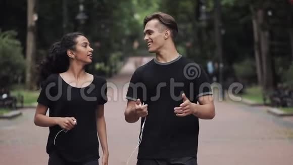 年轻人和音乐女孩微笑着手里拿着耳机在公园里散步看起来很开心视频的预览图