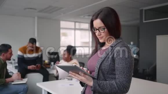 在背景中看到了快乐年轻有魅力的女商人与同事一起使用数码平板电脑的画像视频的预览图