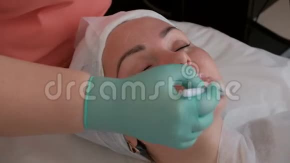 特写镜头美容师用一种滋养凝胶涂在一个漂亮女孩的脸上戴绿色手套的女性Rejj视频的预览图