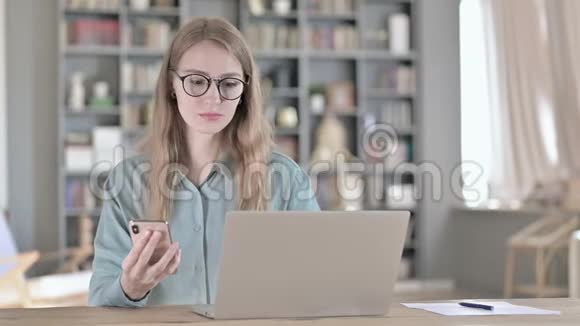 使用智能手机和在笔记本电脑上工作的开朗女人的肖像视频的预览图
