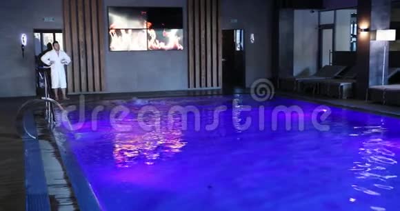 一个男人从他的白袍上跳下准备进入一个昂贵的酒店内的游泳池职业介绍所视频的预览图