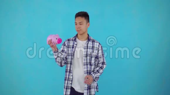 一个体贴的亚洲年轻人手里拿着蓝底的储蓄罐视频的预览图