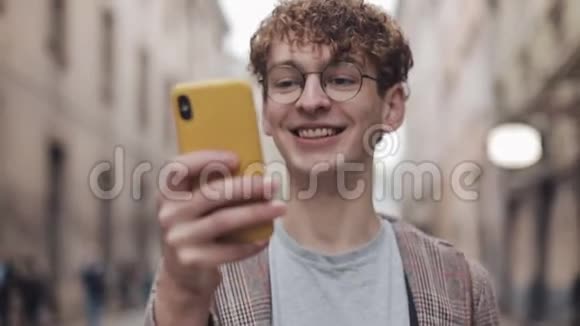 年轻的微笑千禧年在玻璃使用他的智能手机看屏幕而在老城步行与闪烁的电车视频的预览图