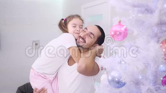 美丽的小女孩拥抱着她的父亲紧紧地拥抱着他的脖子在杉树附近的房子里视频的预览图