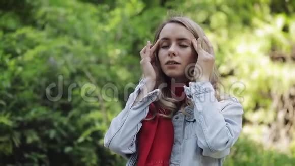 戴着红领巾头痛的年轻女子站在公园里女孩感到不开心偏头痛触动了她视频的预览图