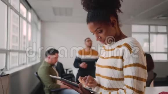 同事在办公室后台互动时用数码平板电脑微笑年轻的非洲女商人视频的预览图