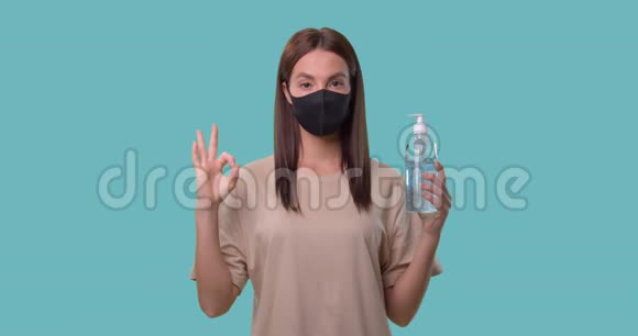 戴着医用口罩的女人手里拿着一个消毒器并显示出一个好的信号被隔离在蓝色上视频的预览图