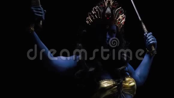 一位印度女神卡莉在一个黑暗的房间里用剑摆姿势的慢镜头视频的预览图