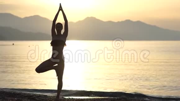 4k女性剪影日出时在海边做瑜伽体式慢动作视频的预览图