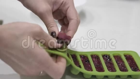 女性的手从一个绿色的硅胶模具从冷冻浆果中提取立方体视频的预览图