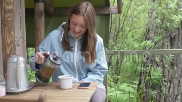 一个女人早上在帐篷附近的树林里喝茶视频的预览图