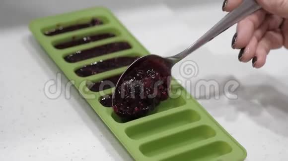 女用手用金属勺子将浆果酱放入绿色硅胶模具中特写视频的预览图