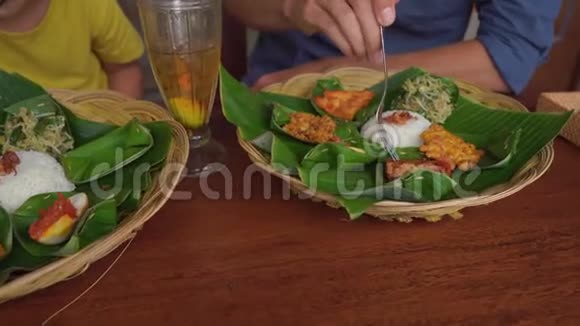 年轻人和他的小儿子在一家传统的咖啡馆里吃传统的巴厘岛食物前往巴厘概念视频的预览图