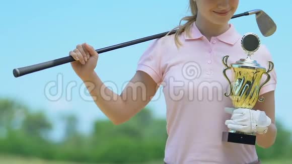 微笑的女孩高尔夫球手摆姿势拿着金杯高兴胜利胜利视频的预览图